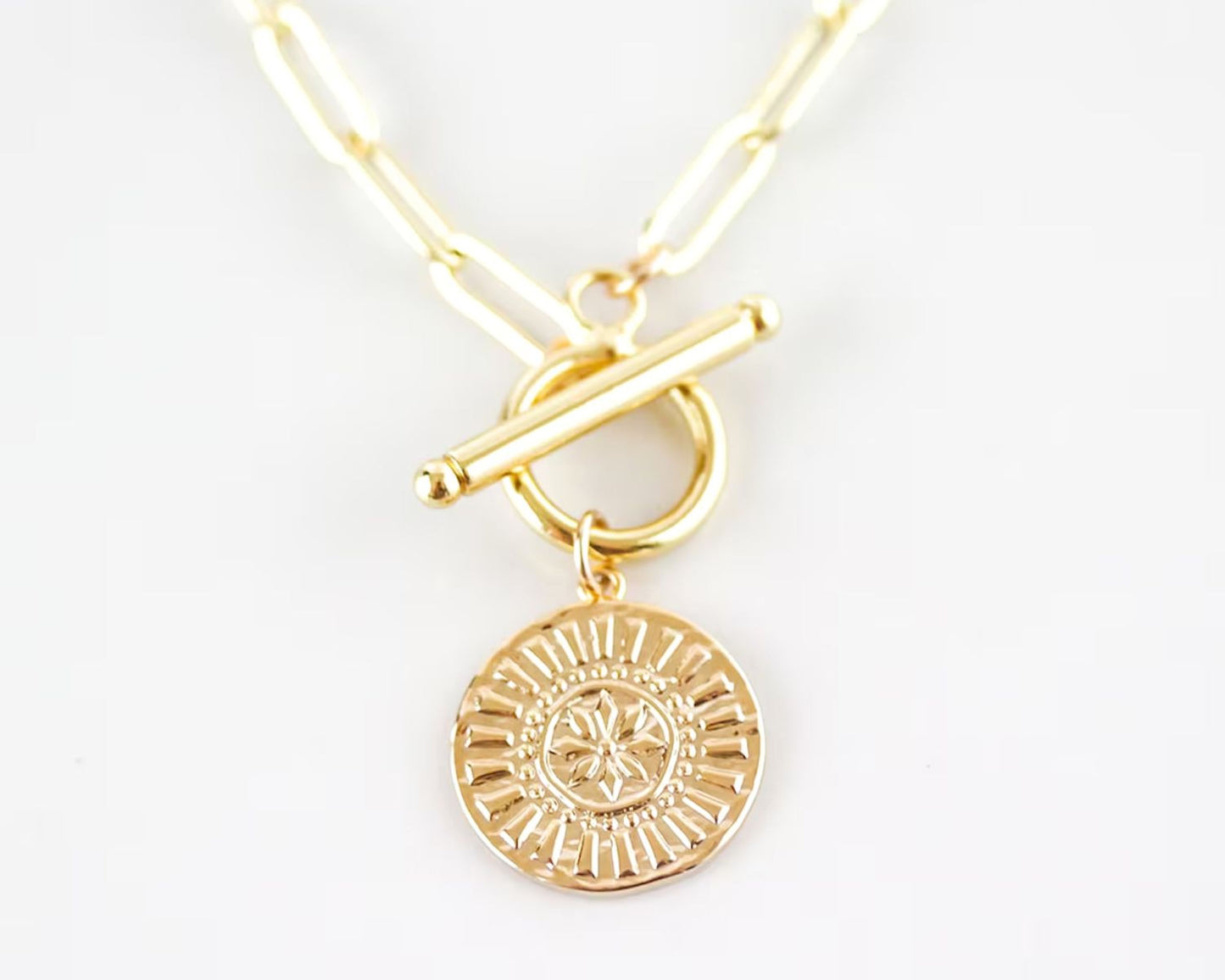 A gold-colored necklace with a circular pendant featuring a floral design.