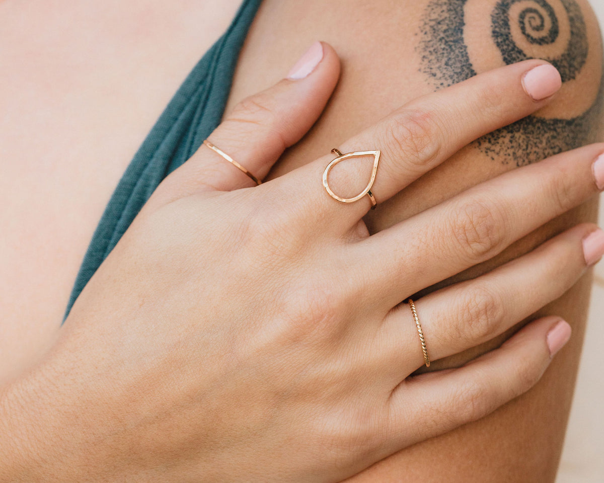 A close-up of a person's hand wearing multiple rings, including a ring with a teardrop design and another ring with a twisted band.