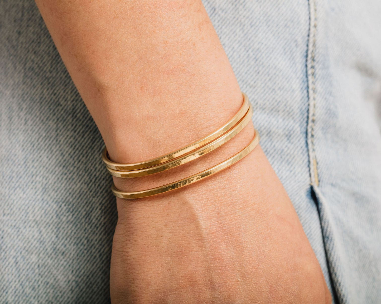 A close-up view of a person's wrist wearing three gold-colored bracelets.