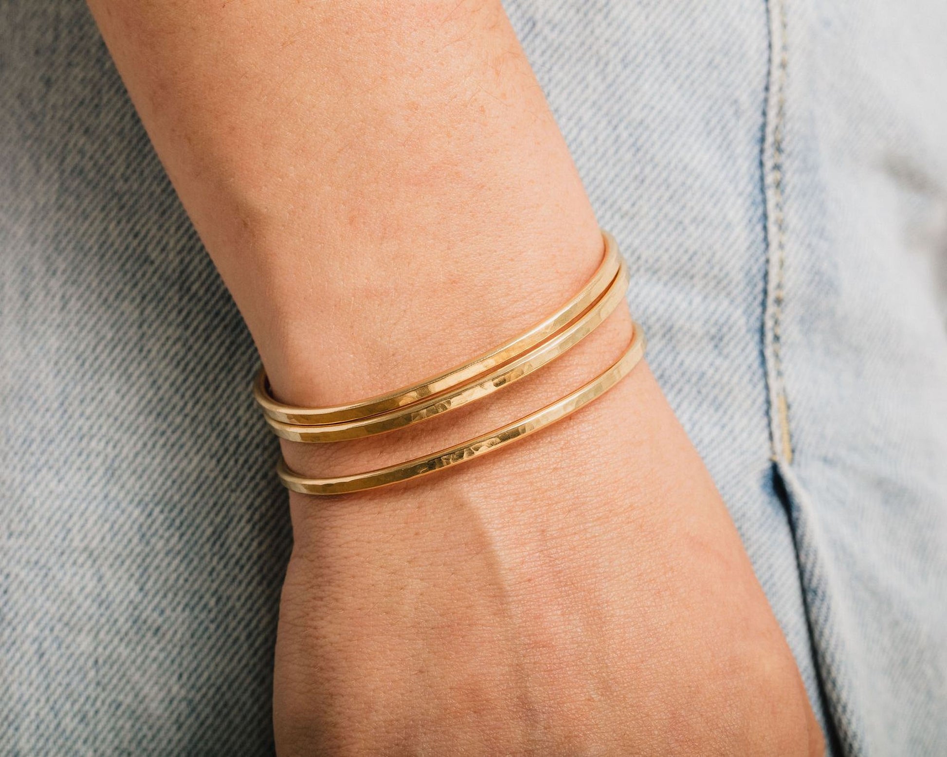 A close-up view of a person's wrist wearing three gold-colored bracelets.