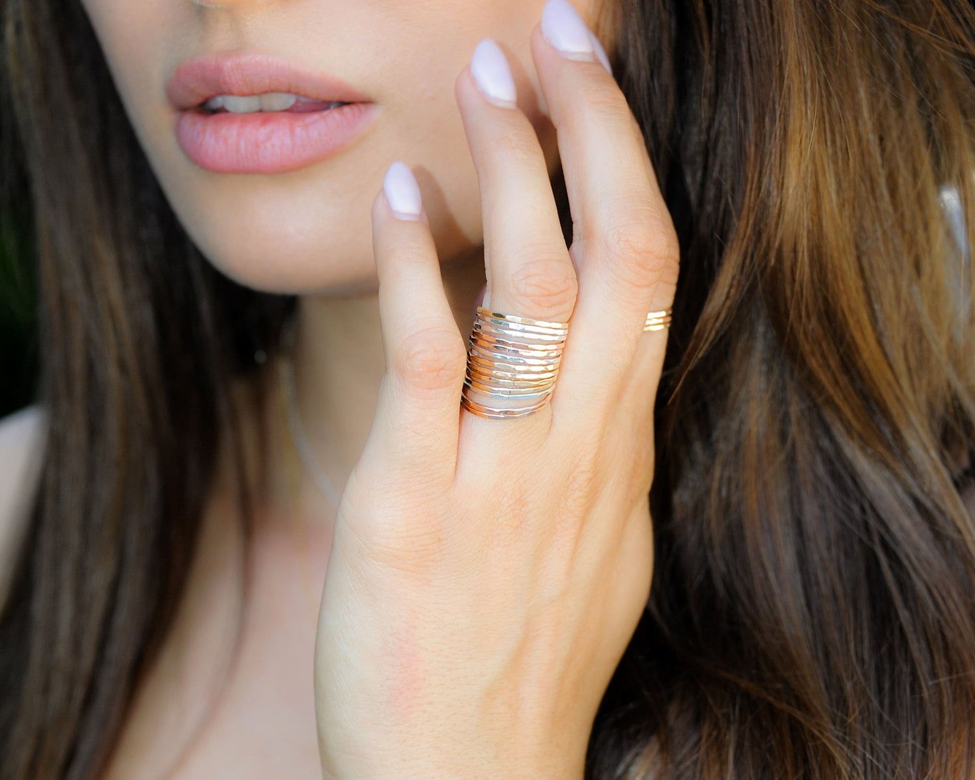 A close-up of a woman's hand wearing multiple rings, with her hair visible in the background.