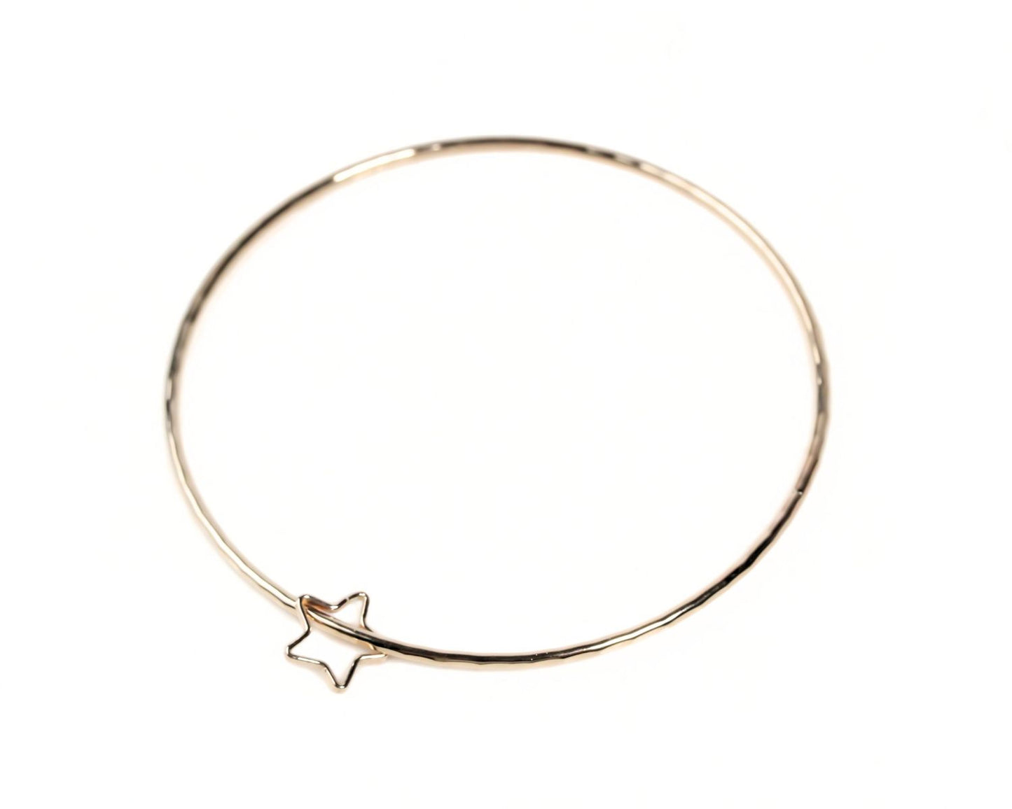A gold-colored bangle bracelet with a star-shaped charm attached to it.