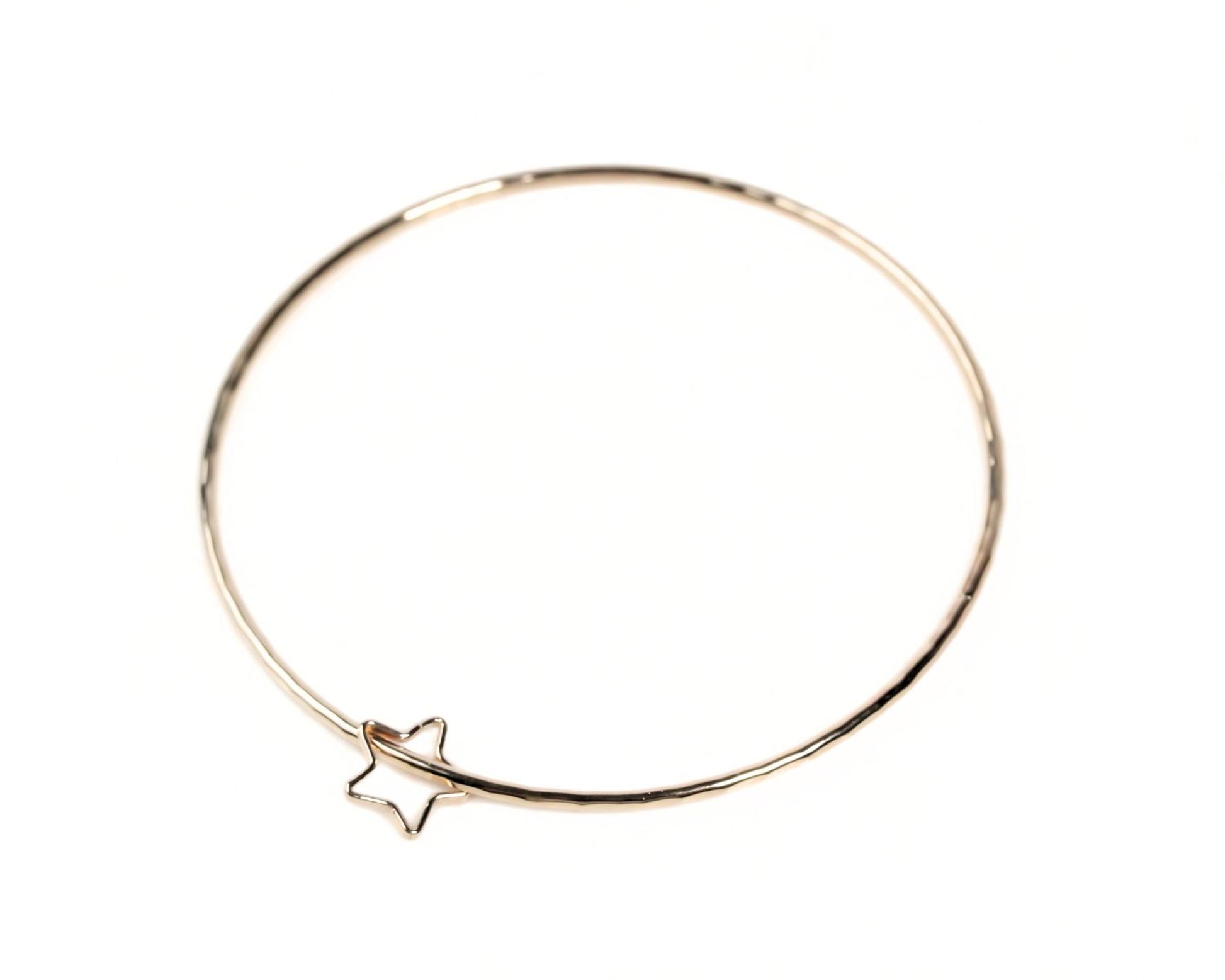 A gold-colored bangle bracelet with a star-shaped charm attached to it.