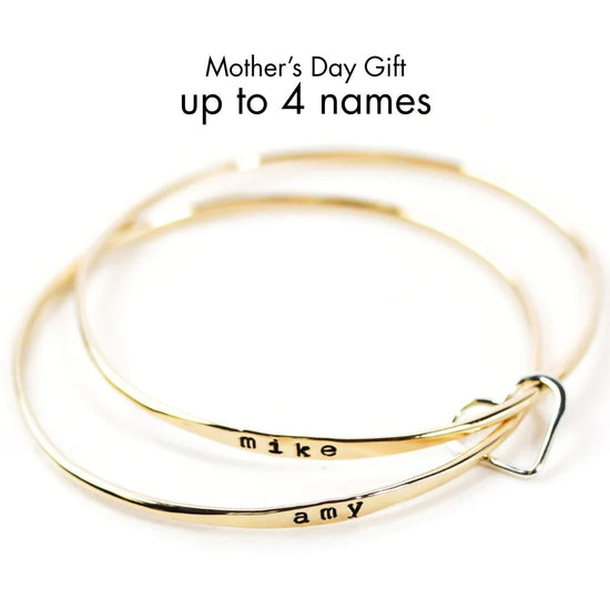 A pair of gold-colored bracelets with personalized names engraved on them, along with a heart-shaped charm.