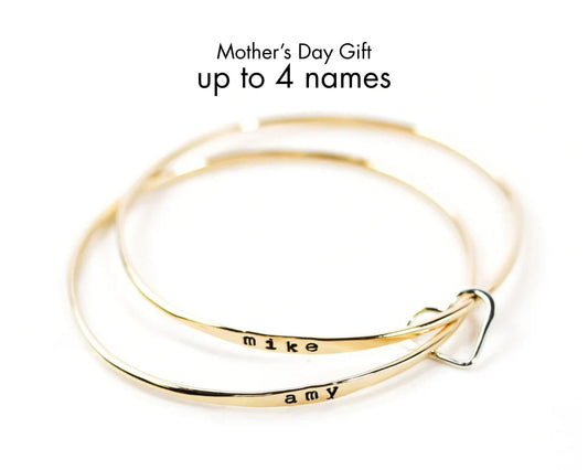 A pair of gold-colored bracelets with personalized names engraved on them, along with a heart-shaped charm.