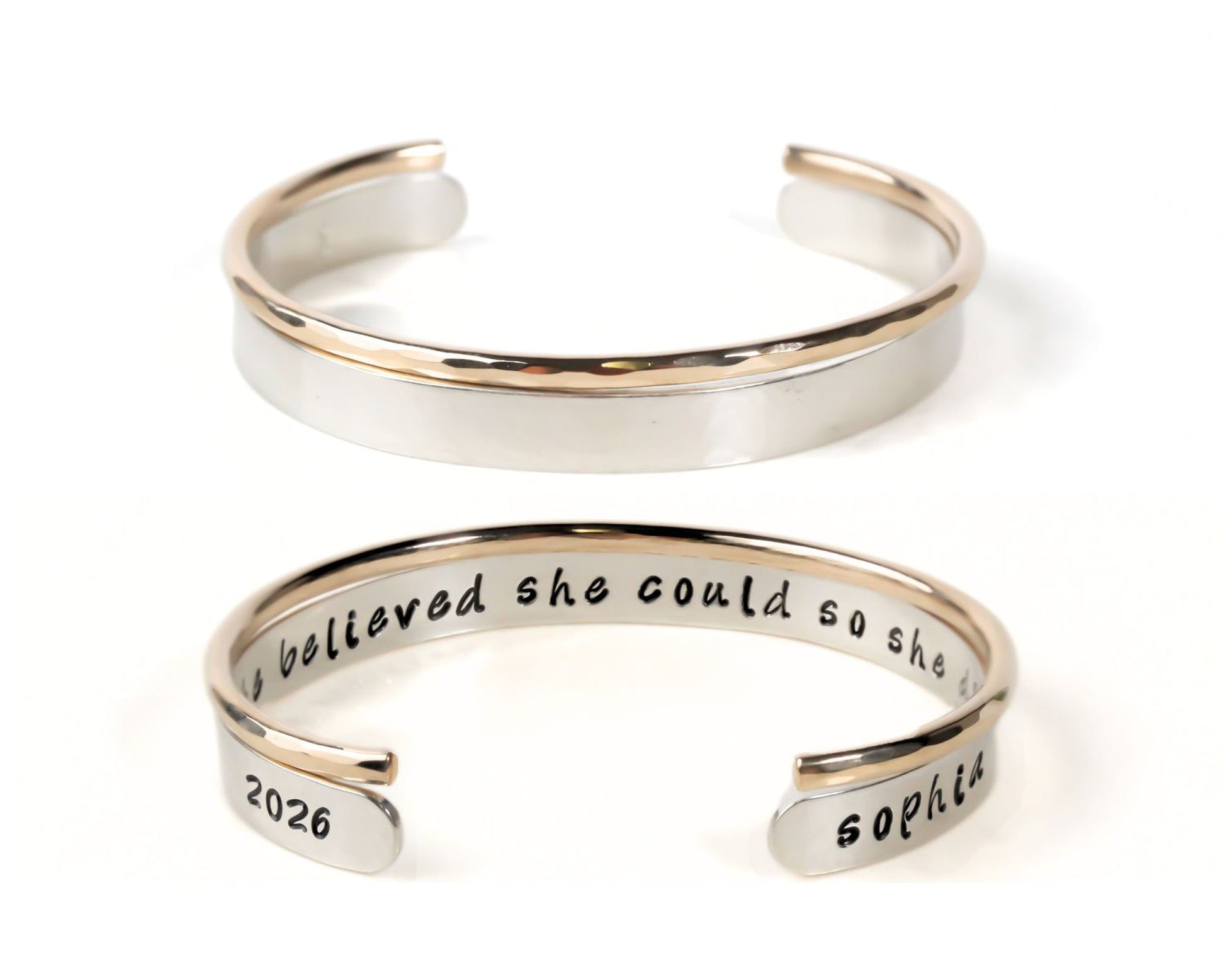 A silver and gold bracelet with the engraved text "I believed she could so she believed she could" on it.