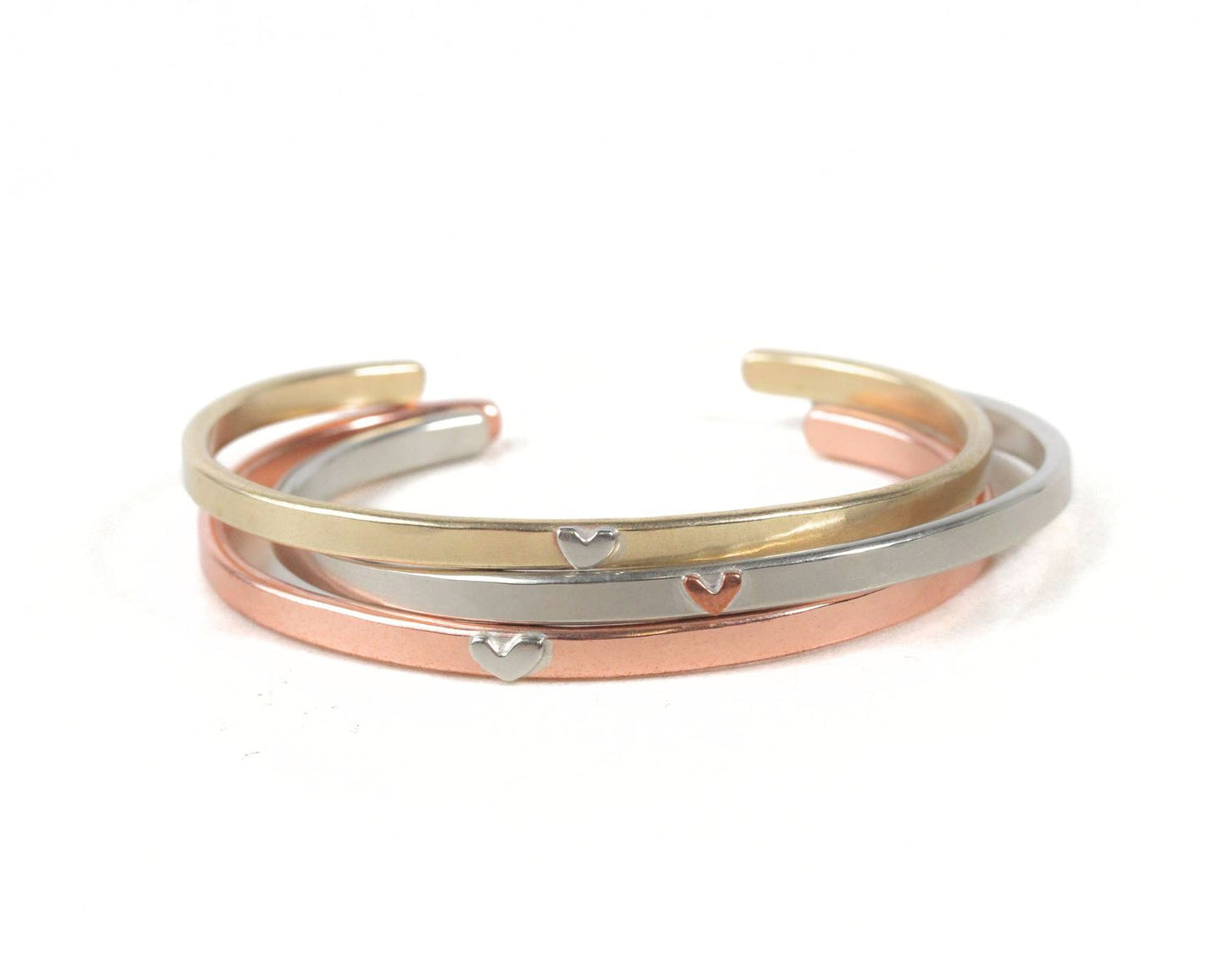 A stack of three bracelets with heart-shaped charms on them.