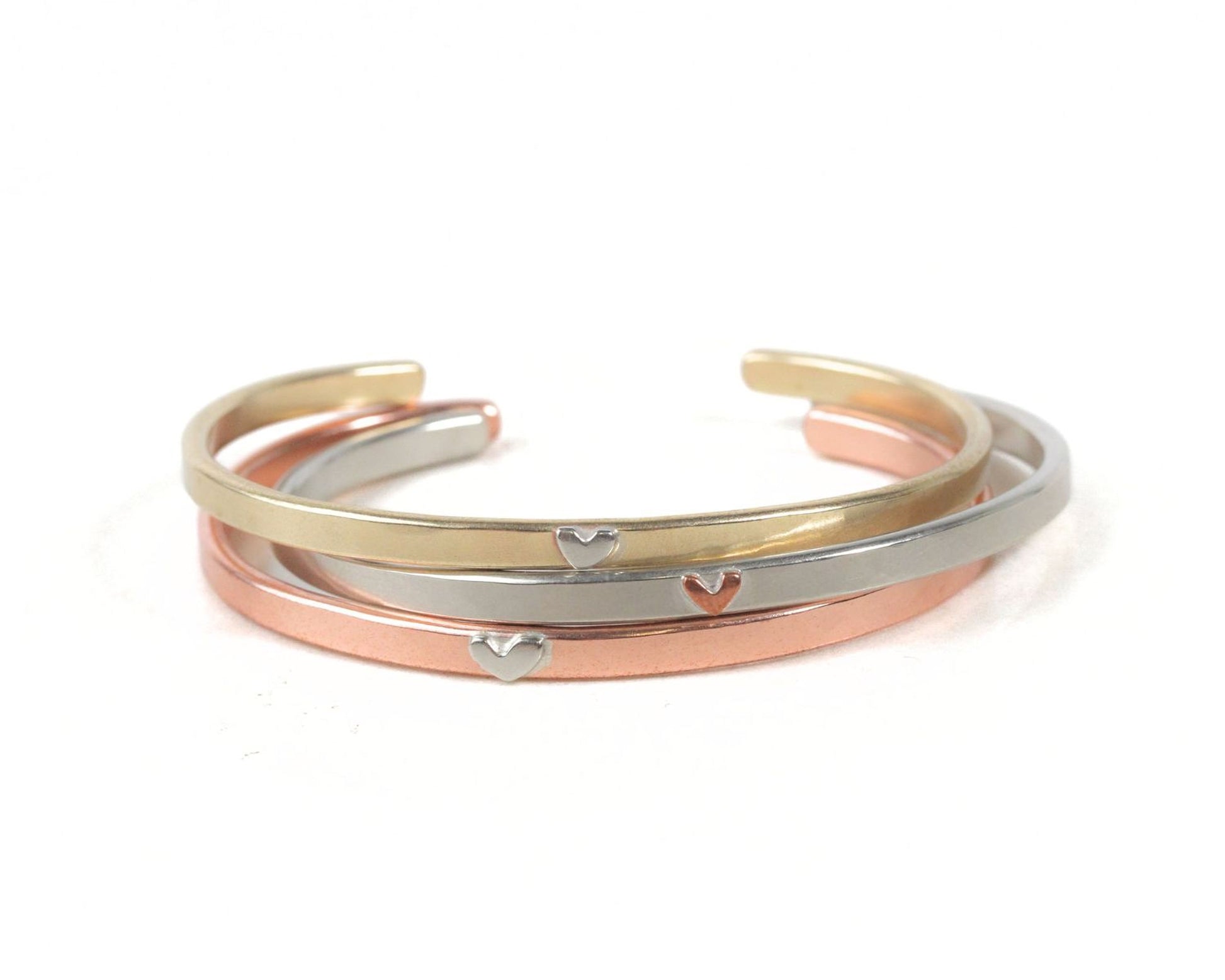 A stack of three bracelets with heart-shaped charms on them.