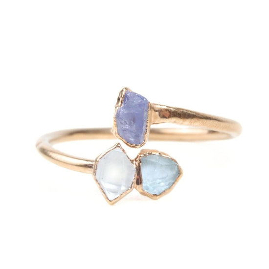A gold ring with two gemstones, one blue and one clear, set in a gold band.