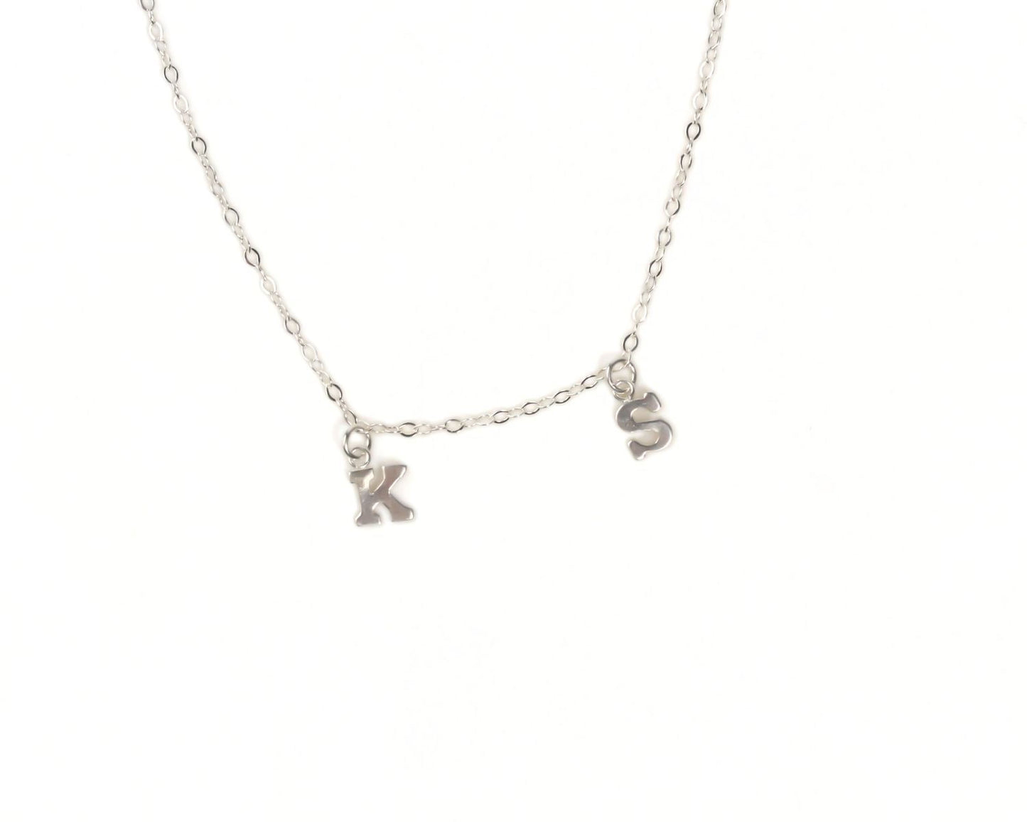 A silver necklace with two small charms hanging from the chain, each representing the letters 'K' and 'S'.