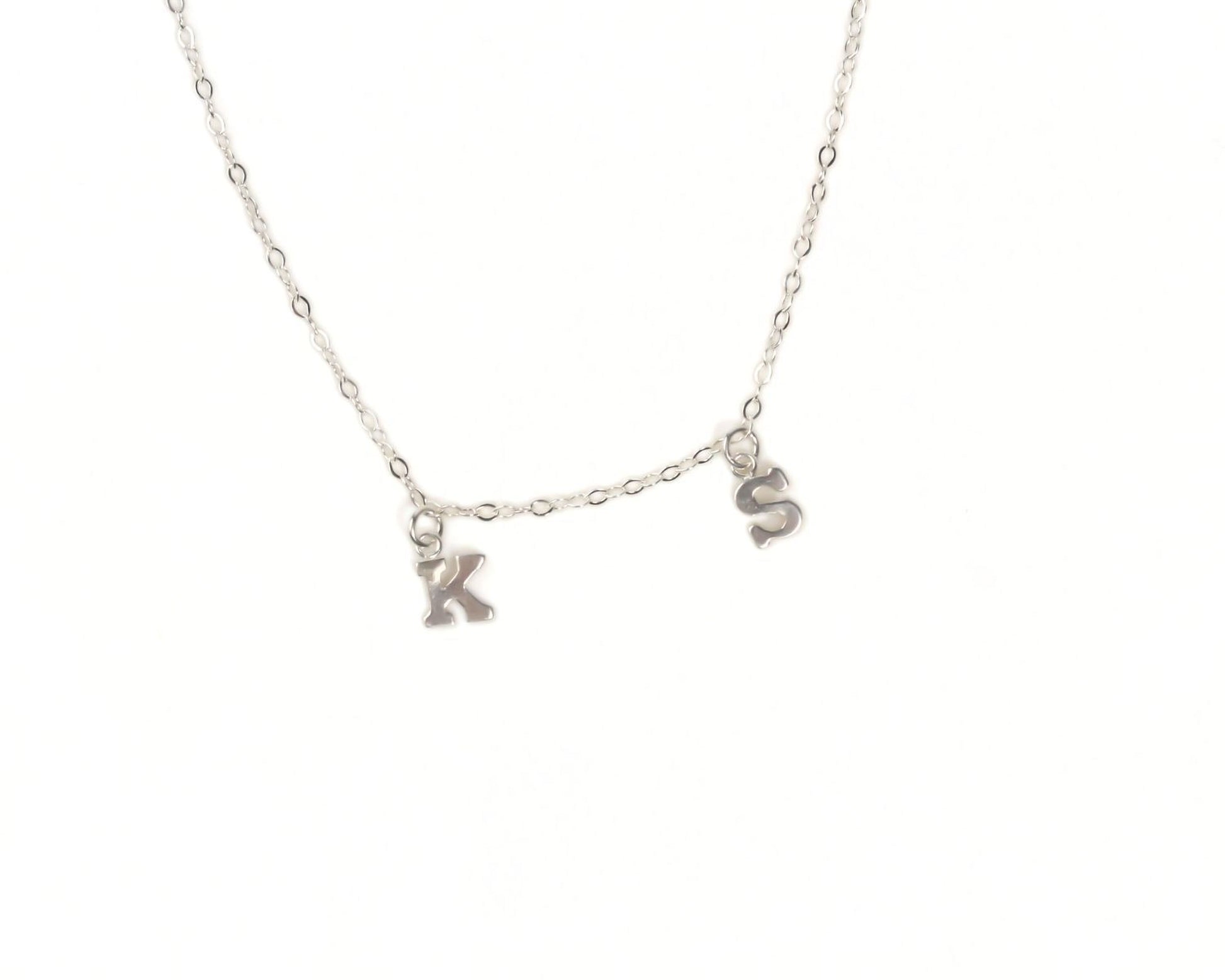 A silver necklace with two small charms hanging from the chain, each representing the letters 'K' and 'S'.