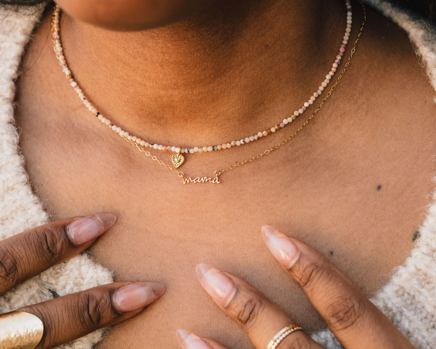A close-up of a person's neck and chest area, featuring a necklace with a heart-shaped charm and the word "mama" engraved on it.