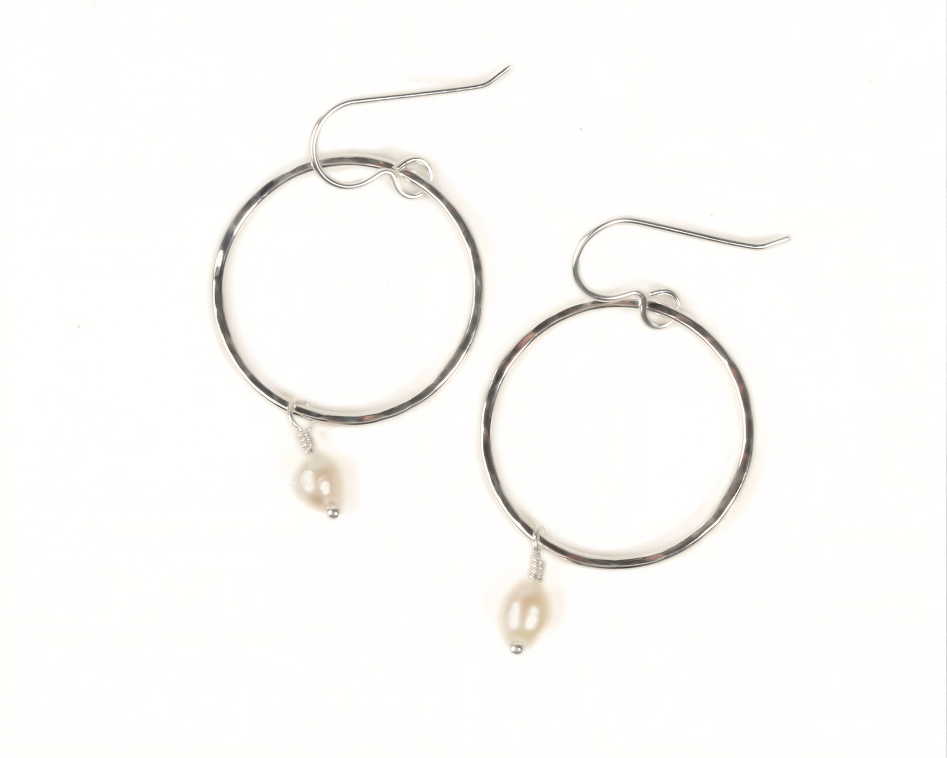 A pair of silver hoop earrings with a single pearl hanging from each.