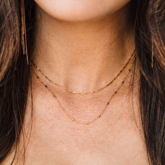 A close-up view of a woman's neck and chest area, showing a delicate gold necklace with multiple strands.