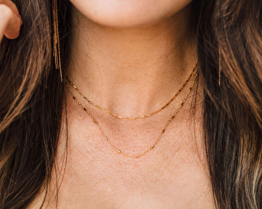 A close-up view of a woman's neck and chest area, showing a delicate gold necklace with multiple strands.