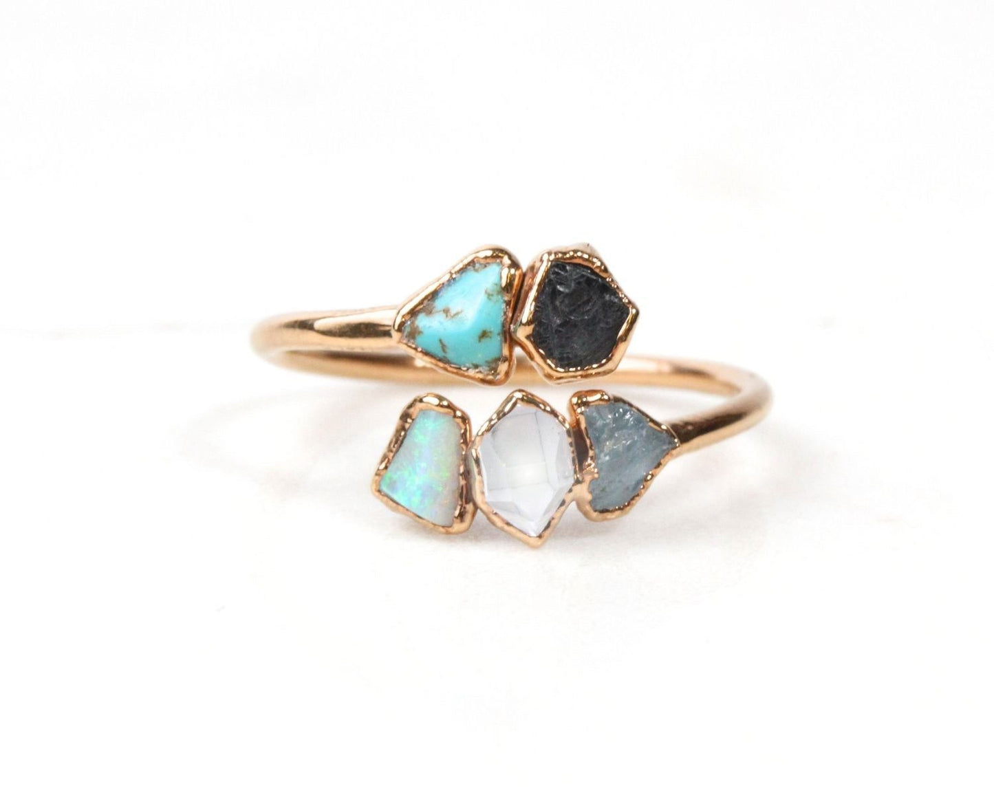 A gold ring with a unique design featuring three different colored gemstones: turquoise, black, and white.