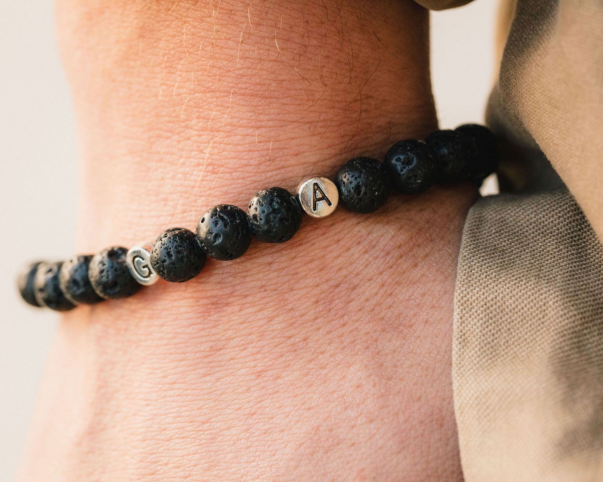 A close-up of a person's wrist wearing a bracelet made of black beads with letters on them.