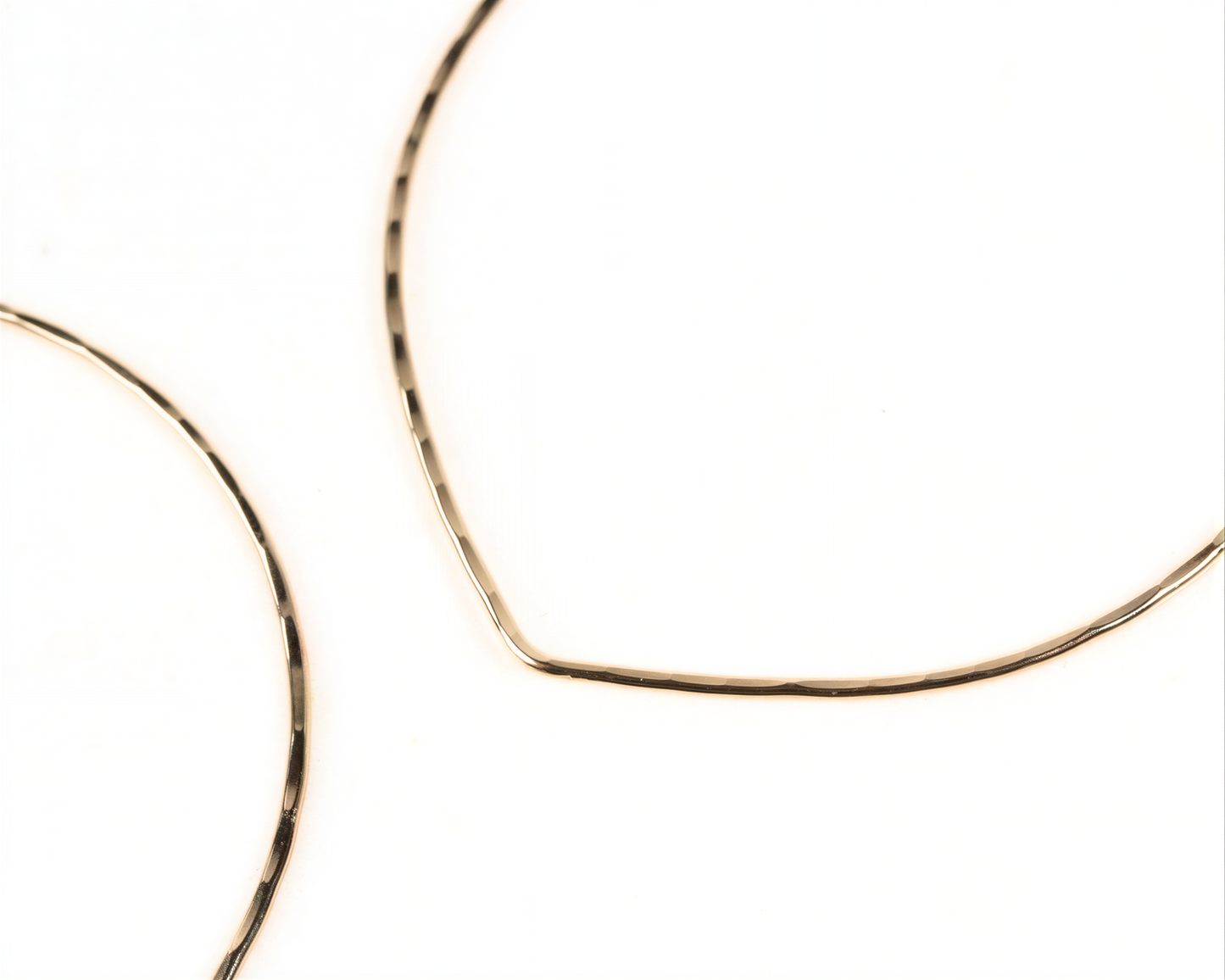 a close-up view of two gold-colored hoop earrings against a white background.