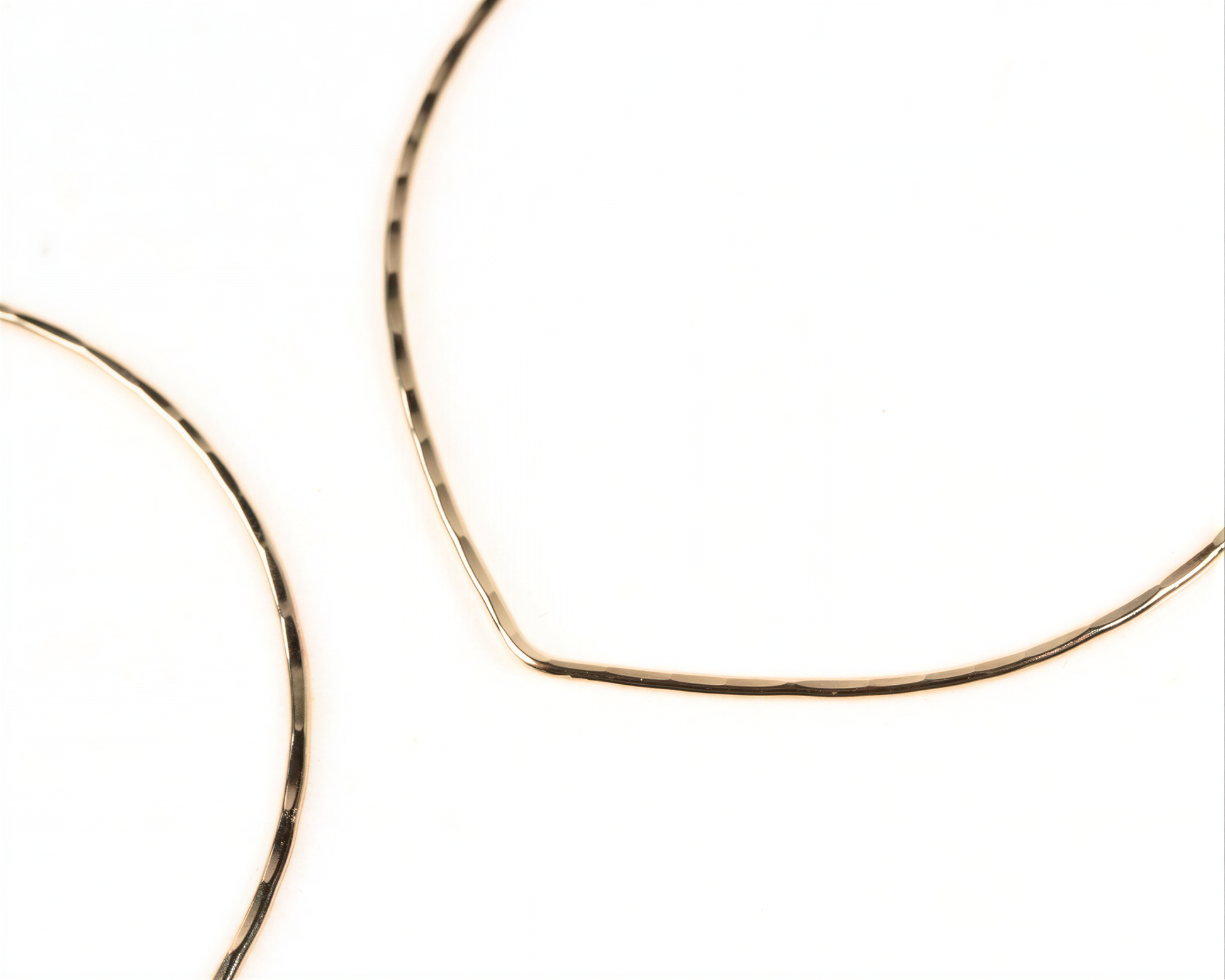 a close-up view of two gold-colored hoop earrings against a white background.