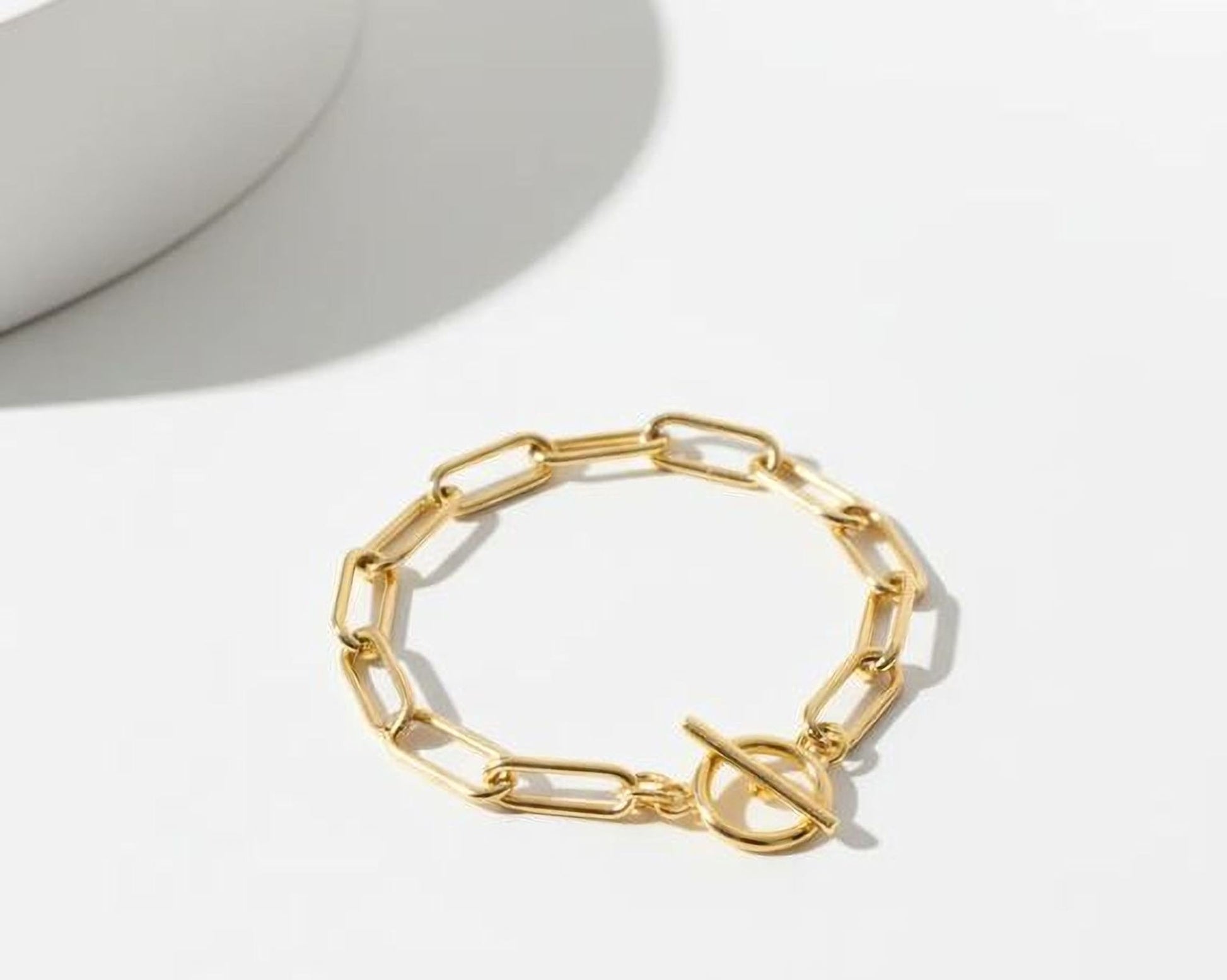 A gold-colored bracelet with a round clasp and a chain-link design, resting on a white surface.