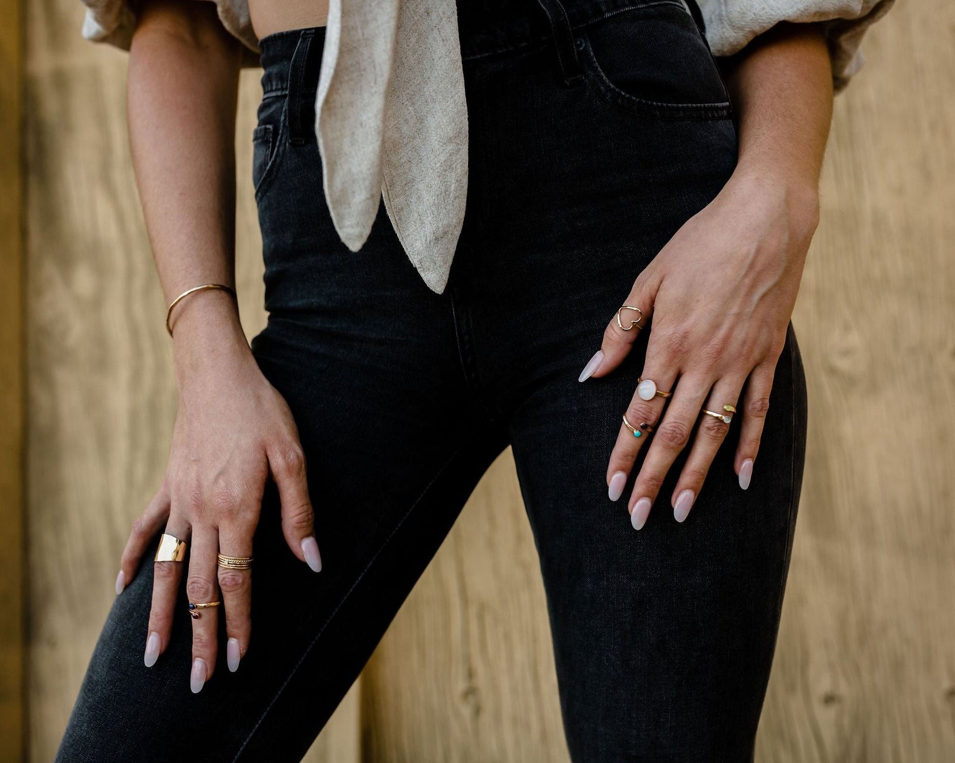 A close-up of a person's hands wearing multiple rings on their fingers, with a wooden background.