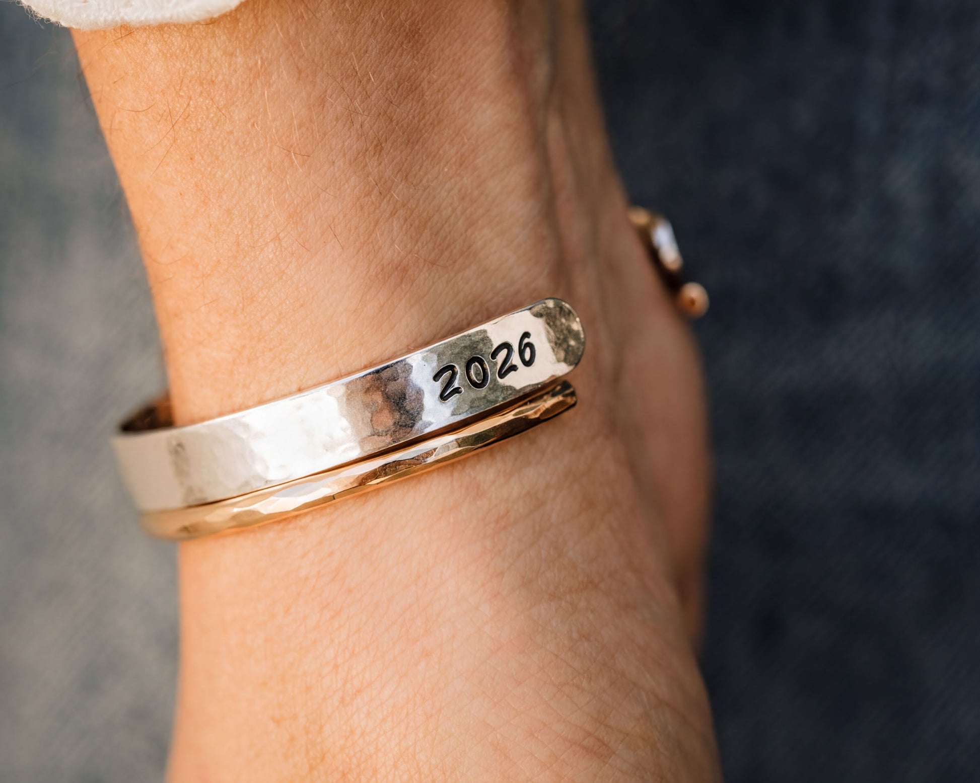 A close-up of a person's wrist wearing a gold-colored bracelet with the year "2026" engraved on it.