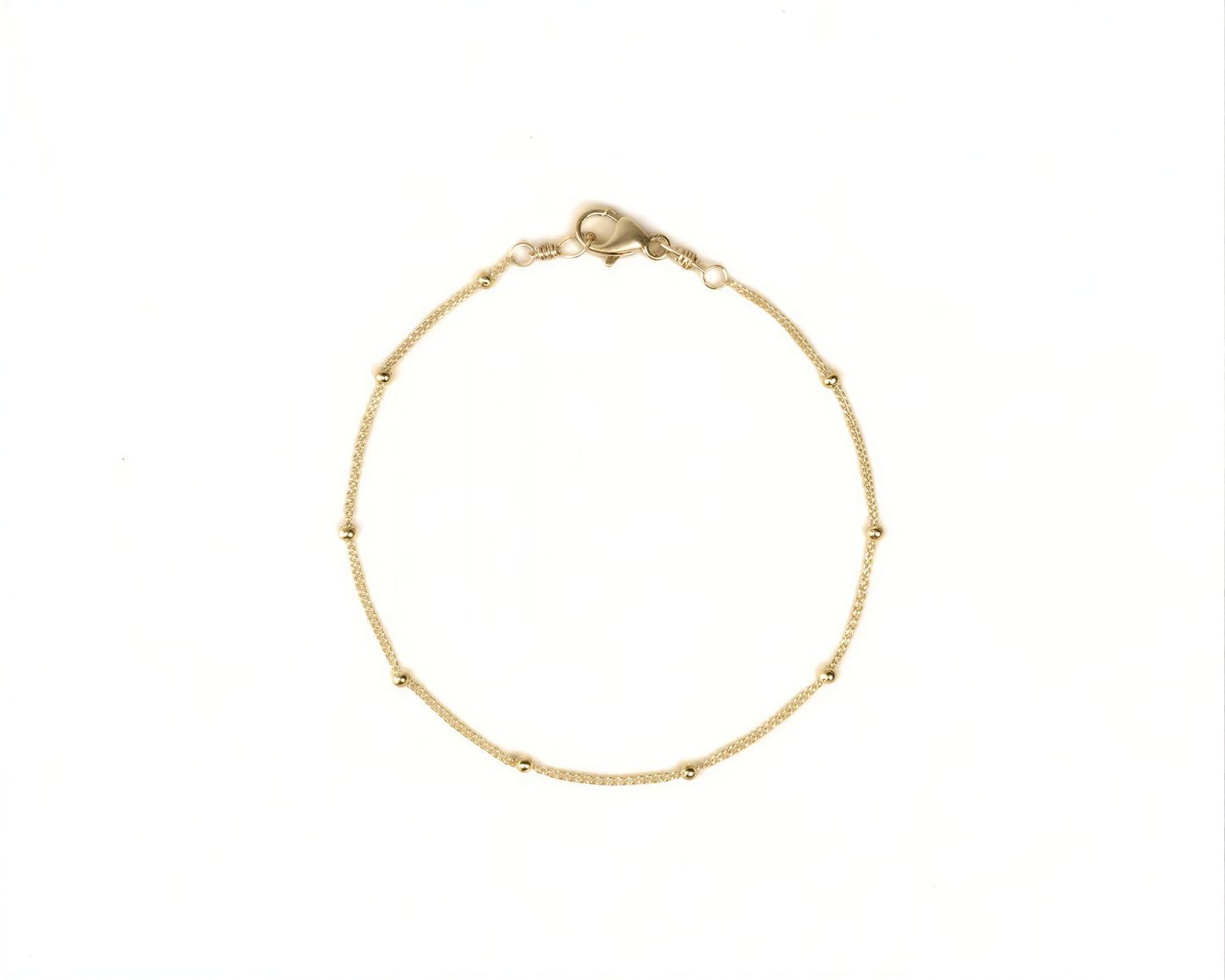 A delicate gold-colored bracelet with small beads on a white background.