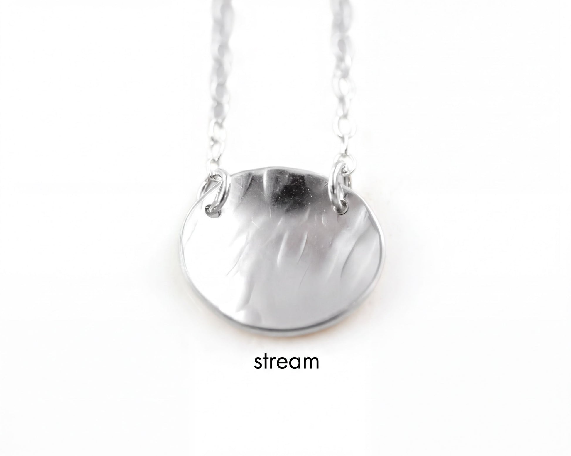 A silver necklace with a round pendant, suspended from a chain.