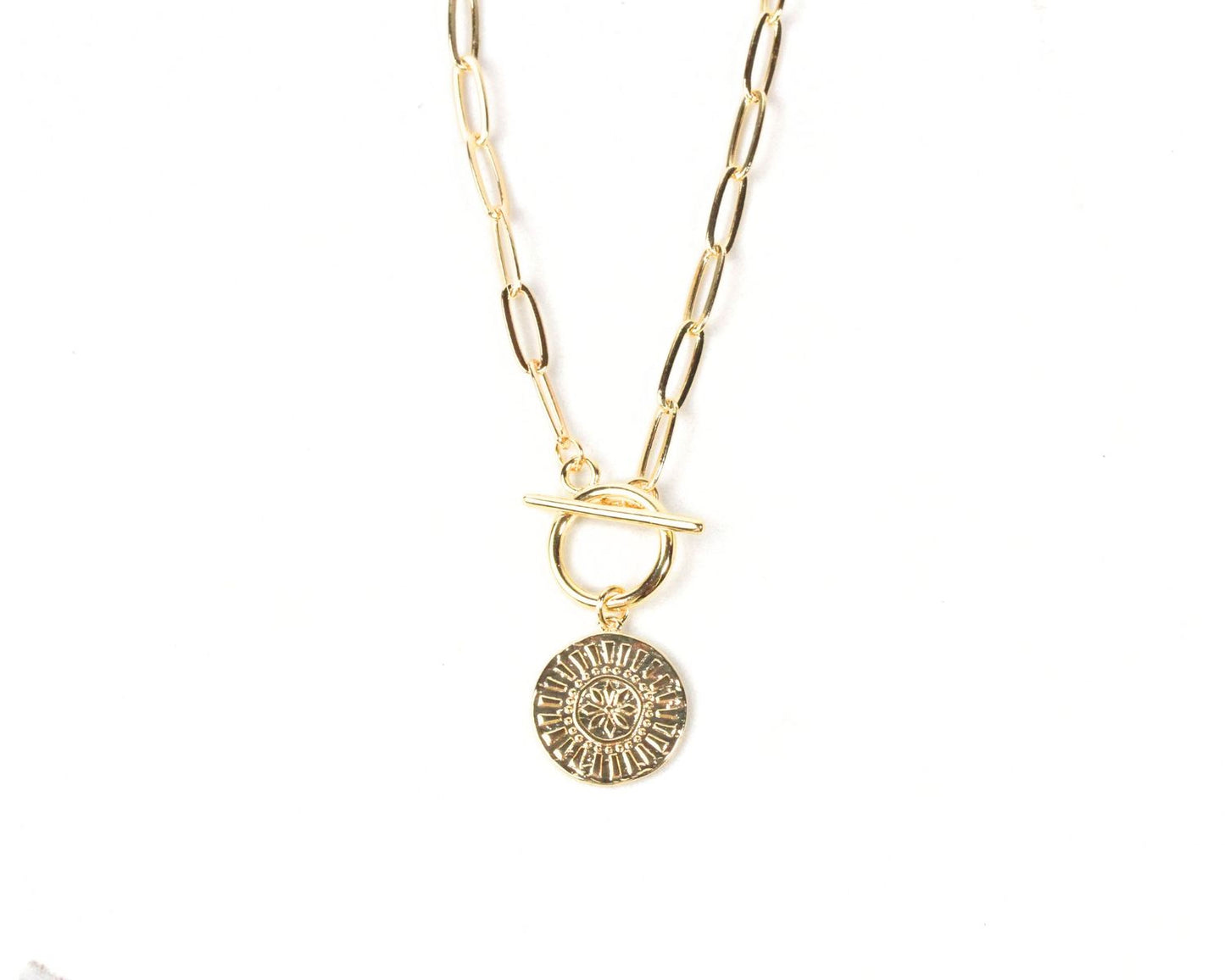 A gold-colored necklace with a round pendant featuring a sun-like design.