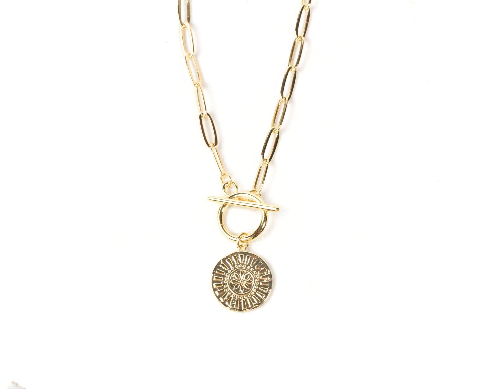 A gold-colored necklace with a round pendant featuring a sun-like design.