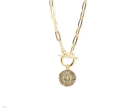 A gold-colored necklace with a round pendant featuring a sun-like design.