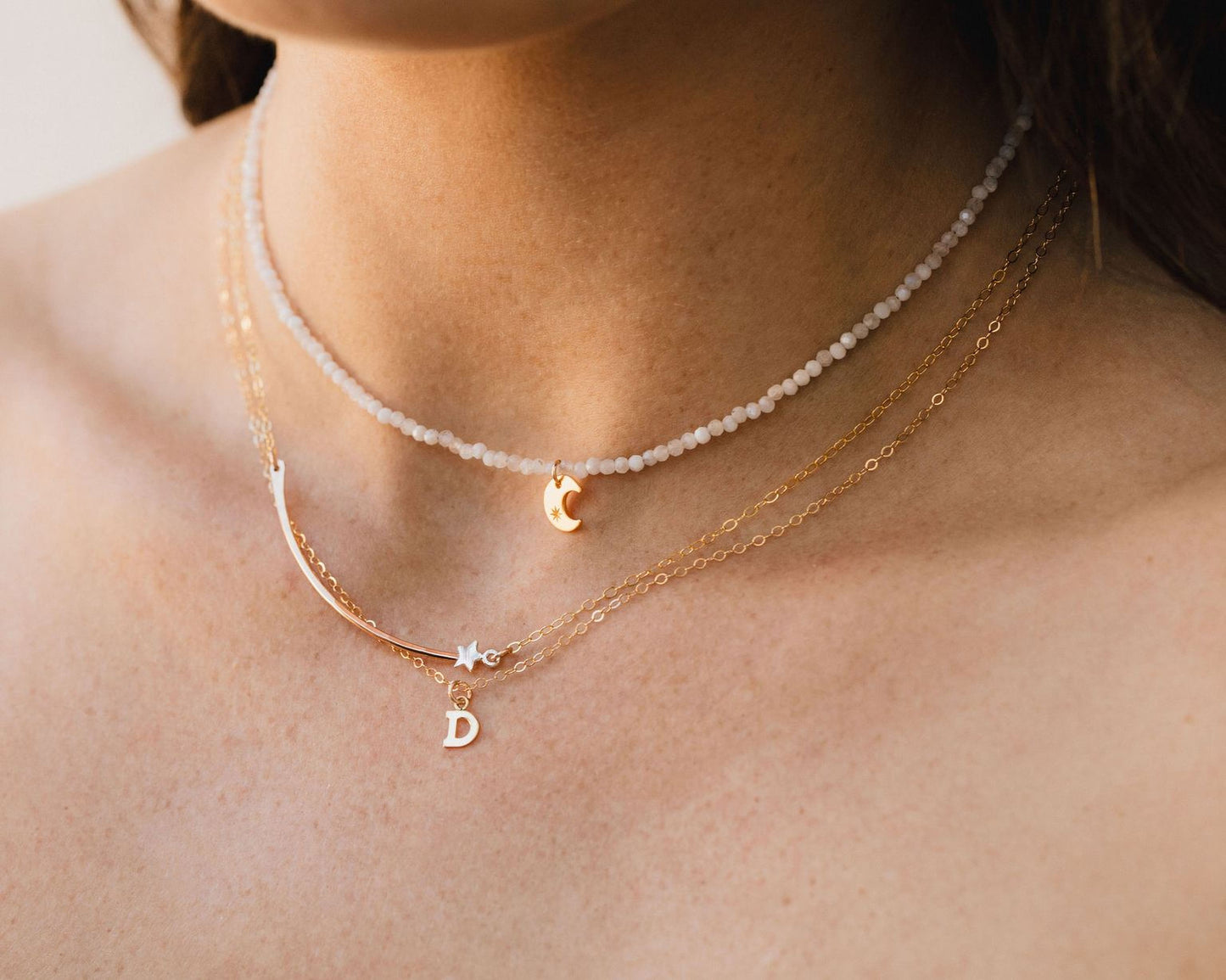 A close-up view of a person's neck adorned with multiple necklaces, including a beaded necklace and a charm necklace.