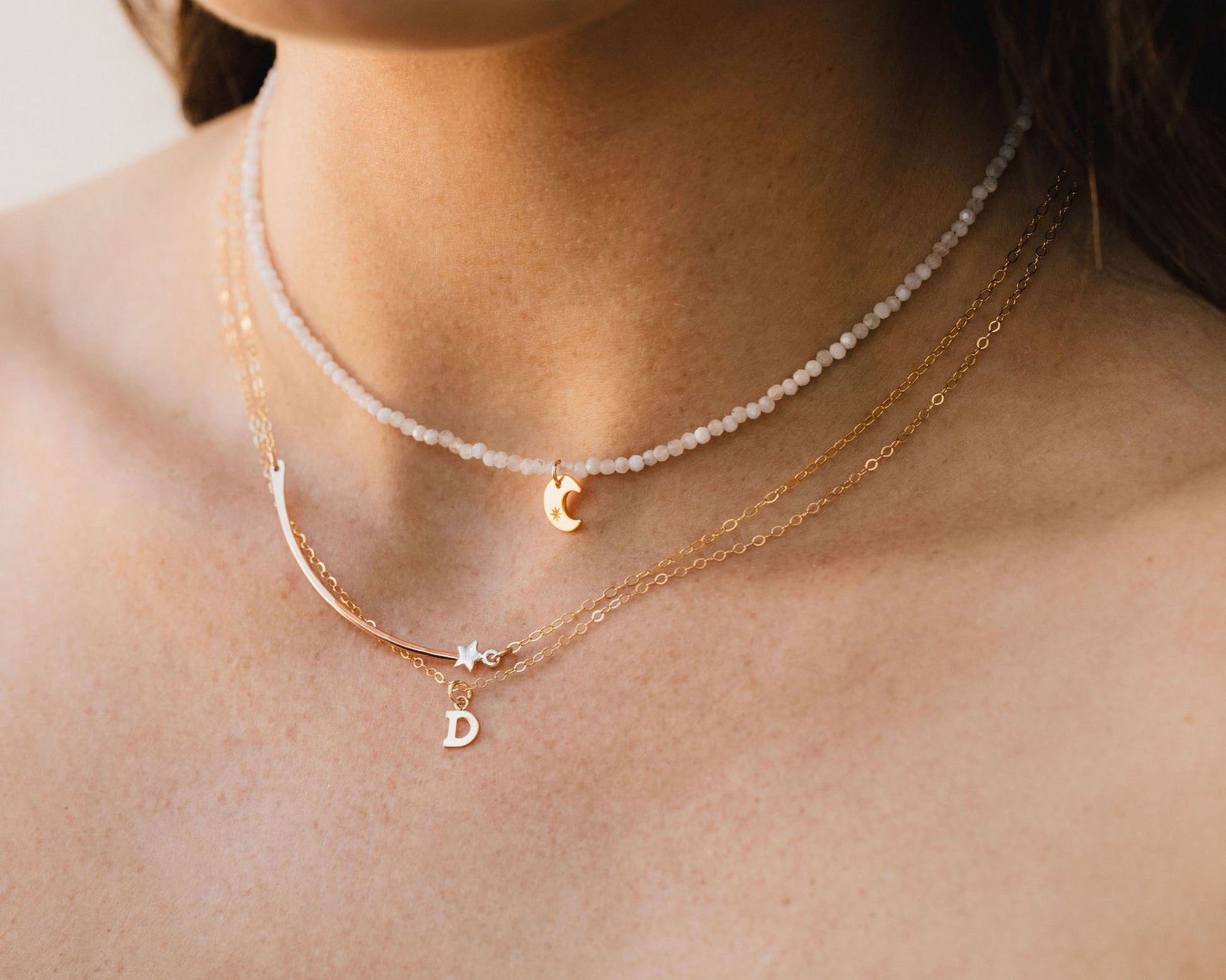 A close-up view of a person's neck adorned with multiple necklaces, including a beaded necklace and a charm necklace.
