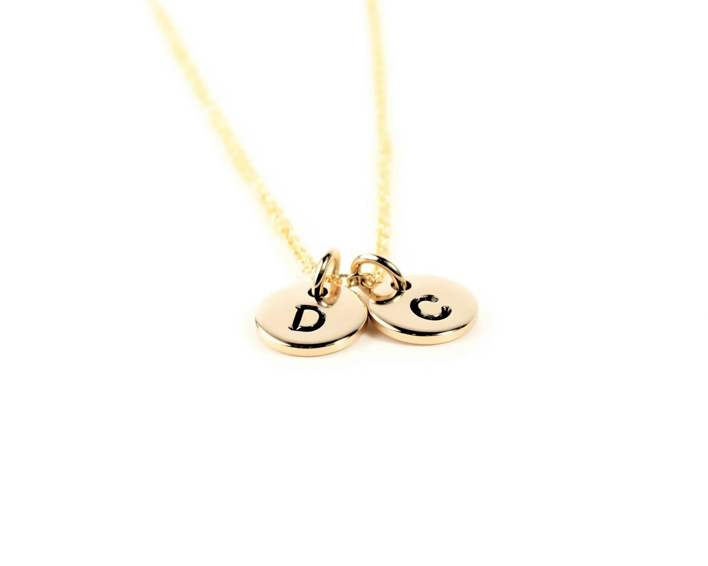 A gold-colored necklace with two round charms attached to it, each with a letter engraved on it.