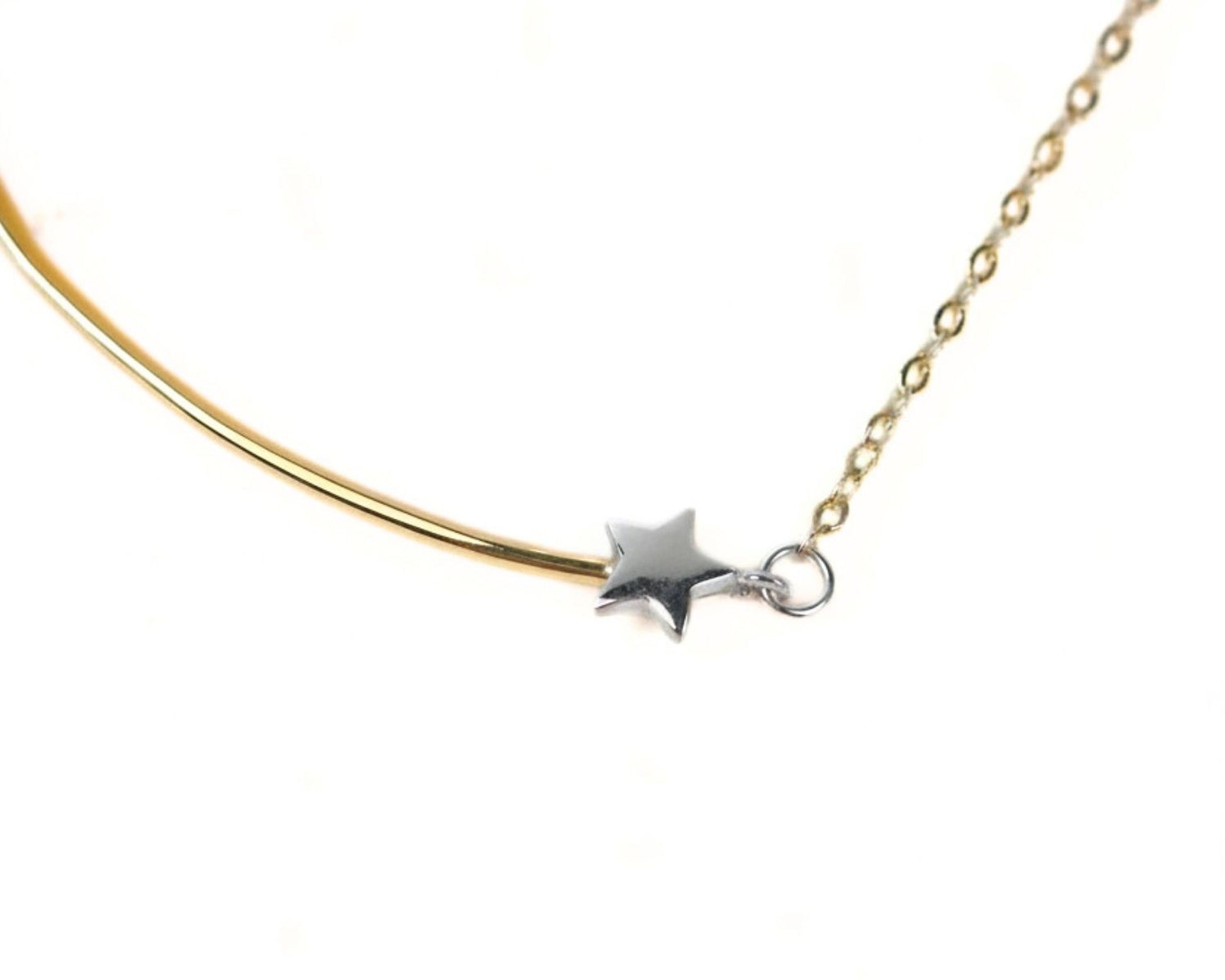 A close-up view of a necklace with a gold-colored metal bar and a silver star-shaped charm attached to it.