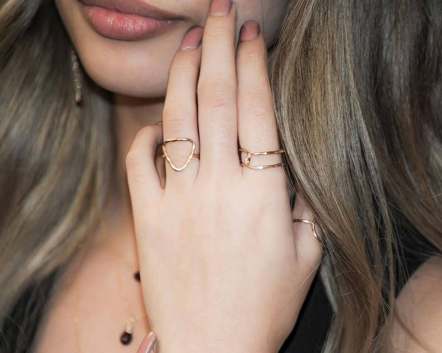A close-up of a person's hand wearing multiple rings, with their fingers partially obscured by the rings.