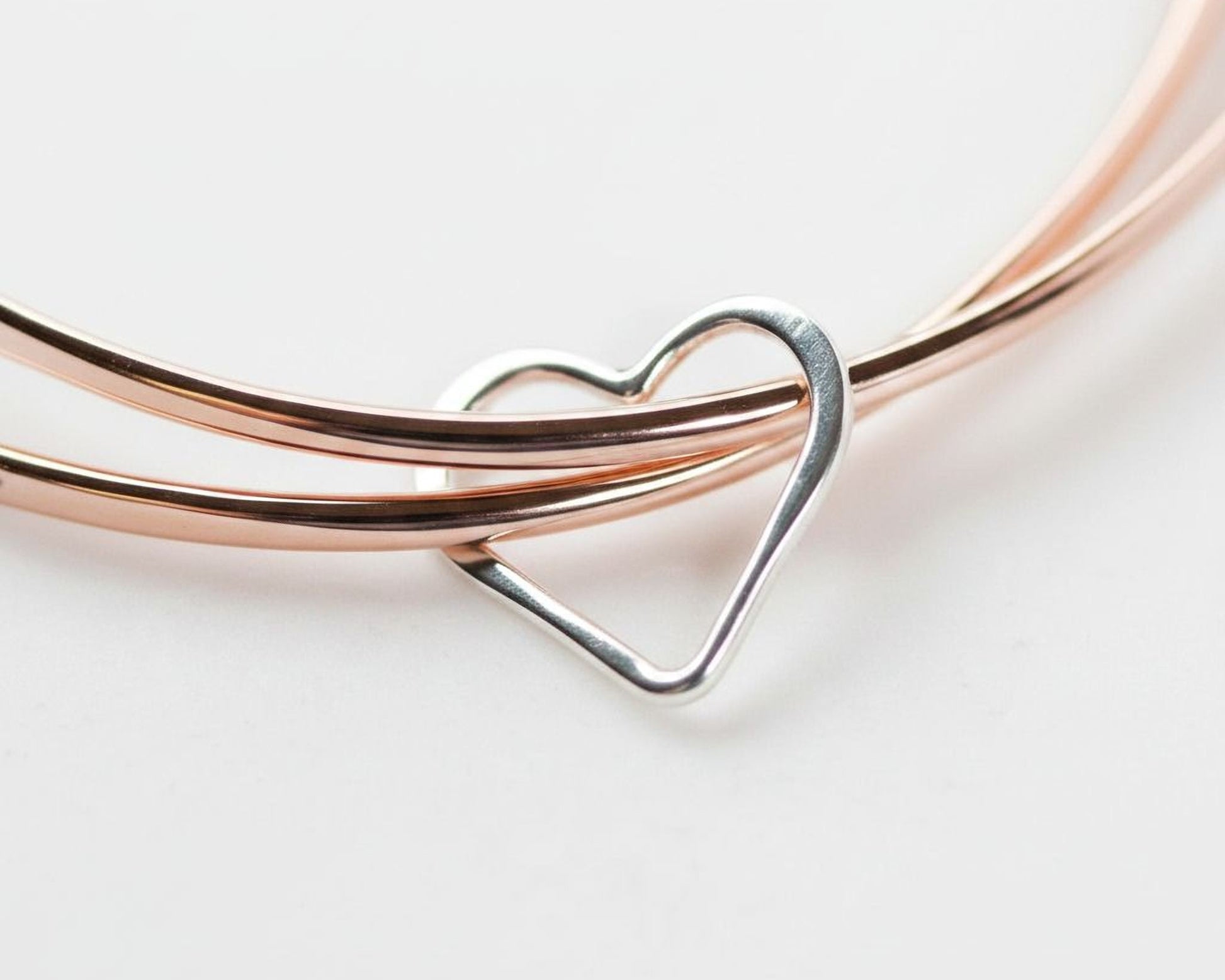 A silver heart-shaped charm is attached to a bracelet made of copper-colored metal.