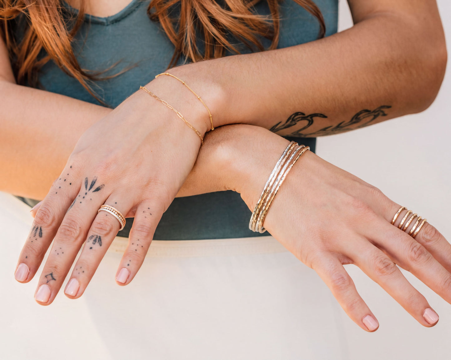 A close-up of a person's hands wearing multiple rings and bracelets, with tattoos visible on their fingers.
