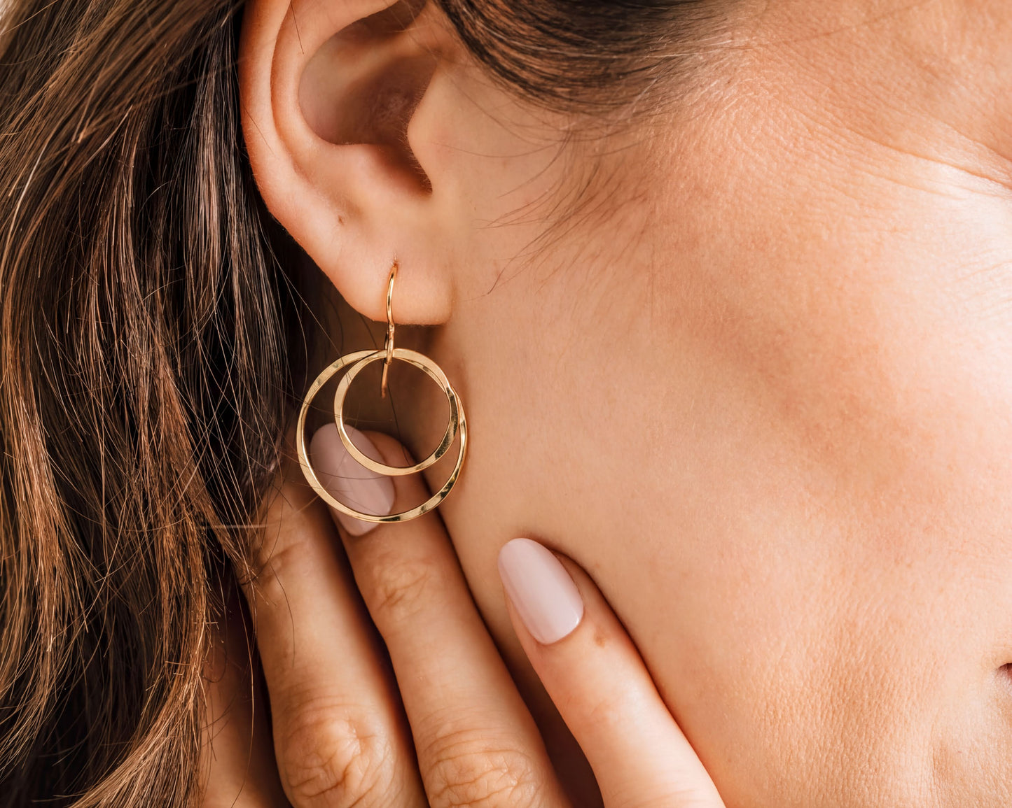 A close-up of a person's ear wearing a gold hoop earring with a circular design.
