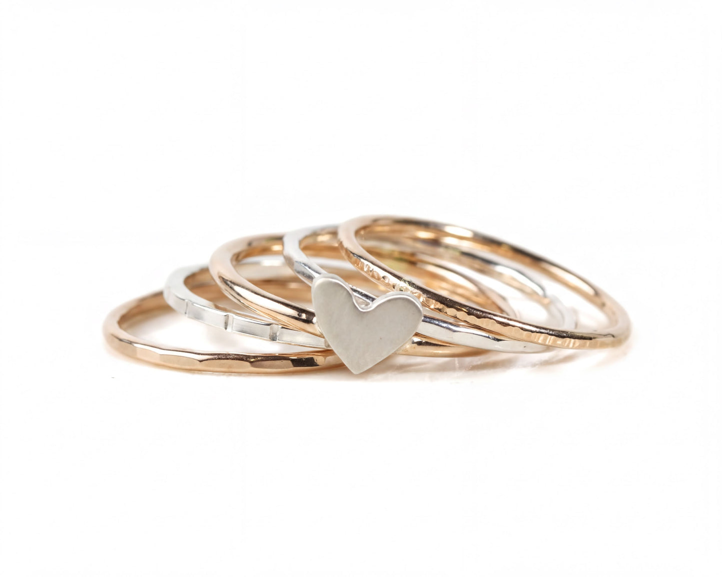 A stack of gold and silver rings with a heart-shaped charm in the center.