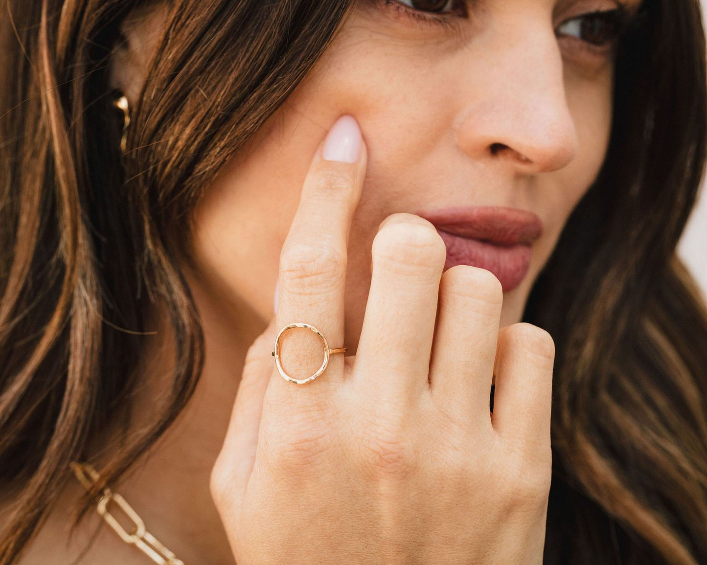A close-up of a woman's face, focusing on her hand and finger adorned with a ring.