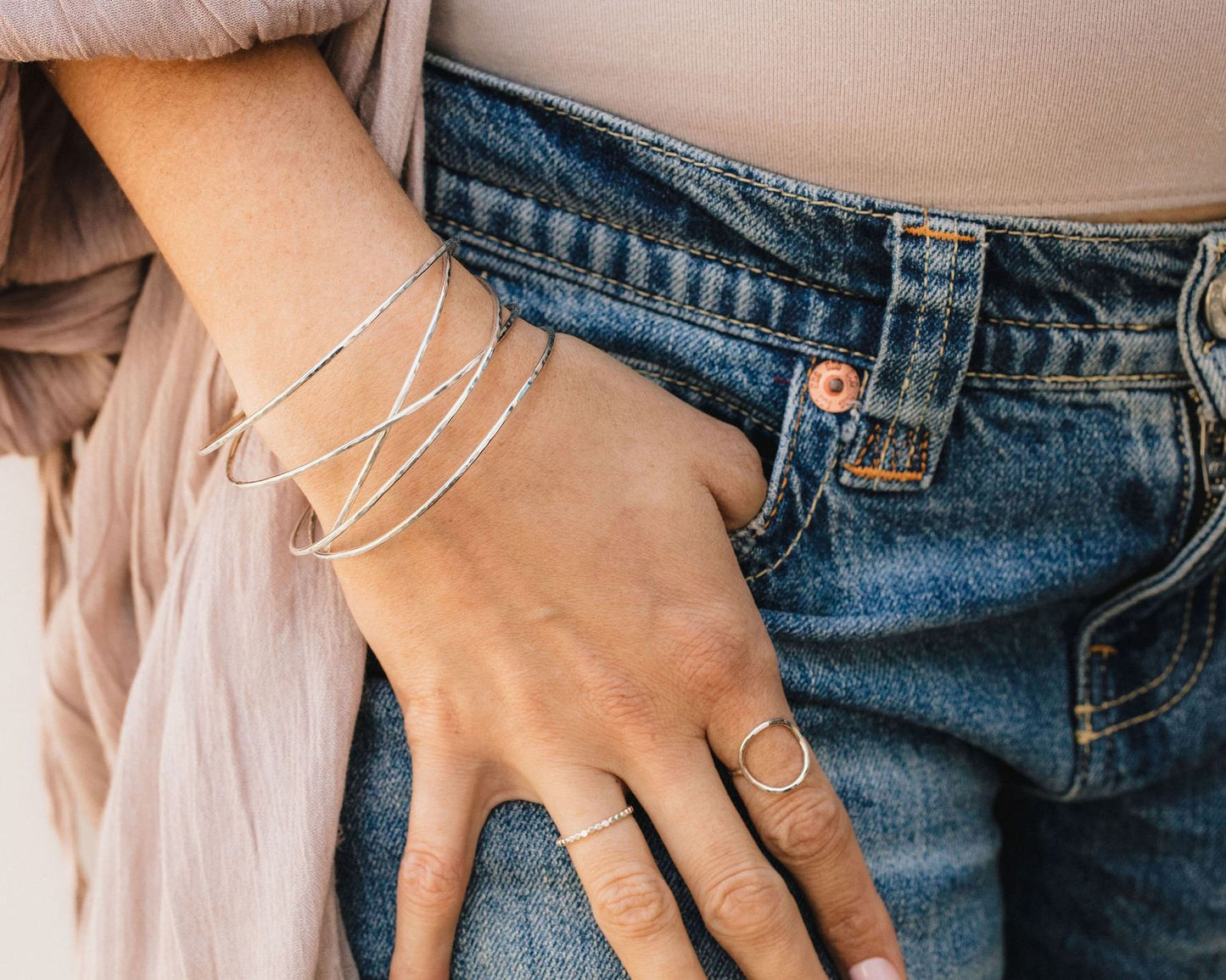 A close-up view of a person's hand wearing multiple bracelets and rings, with a denim-style pocket on the jeans.