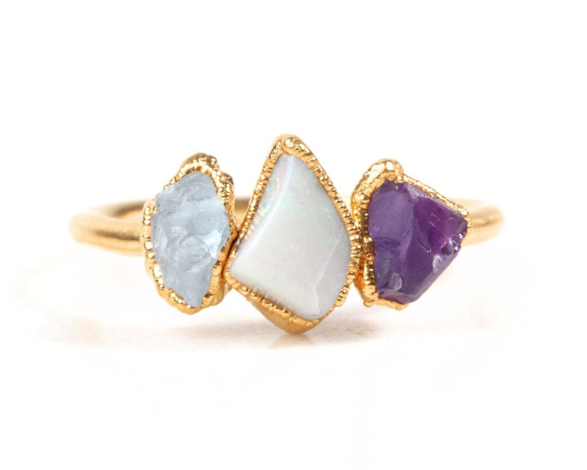 A gold ring with three gemstones: a white opal, a purple amethyst, and a blue sapphire.