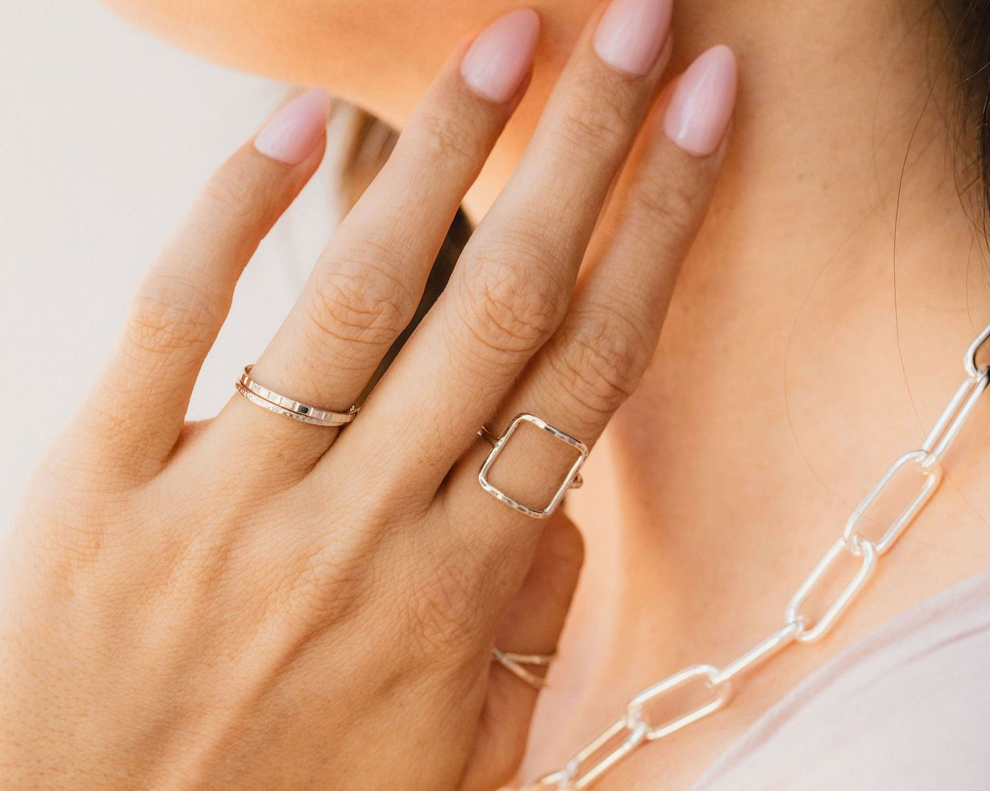 A close-up of a person's hand wearing multiple rings, including a ring with a square cut design and another ring with a thin band.