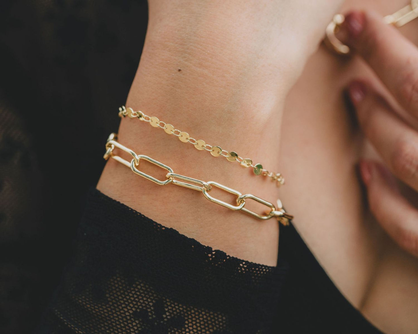 A close-up view of a person's wrist wearing two gold-colored bracelets, one with a chain-link design and the other with a round-shaped charm.