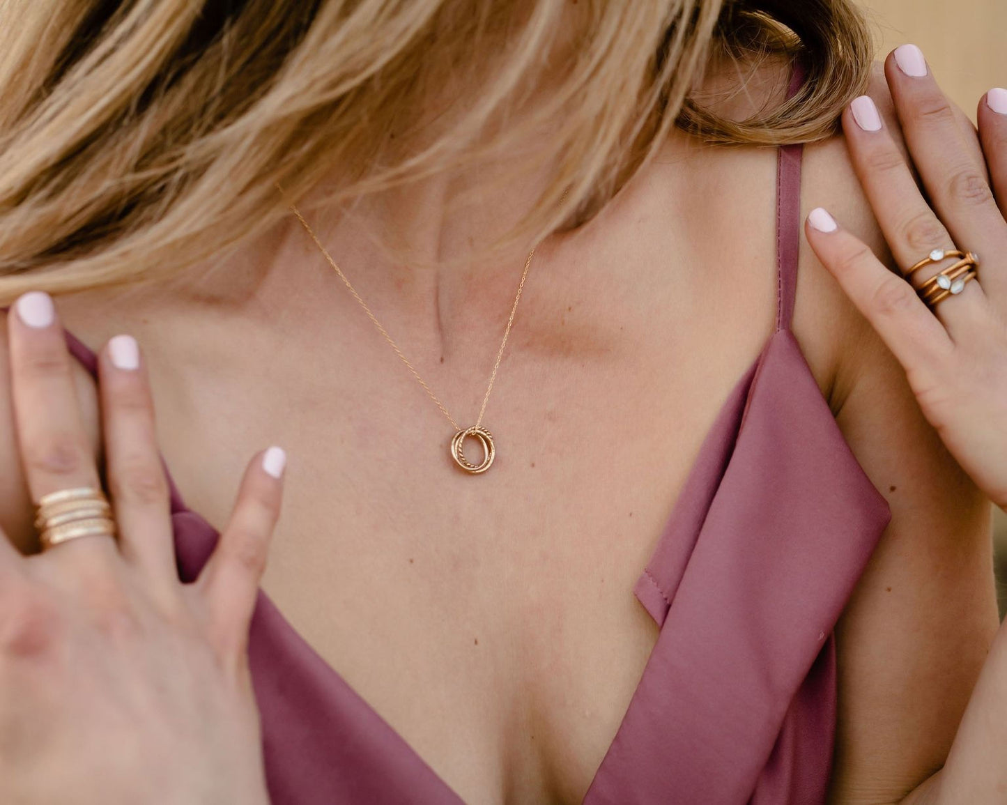 A close-up view of a woman's neck and chest area, showing a gold necklace with a pendant and her hands adorned with rings.