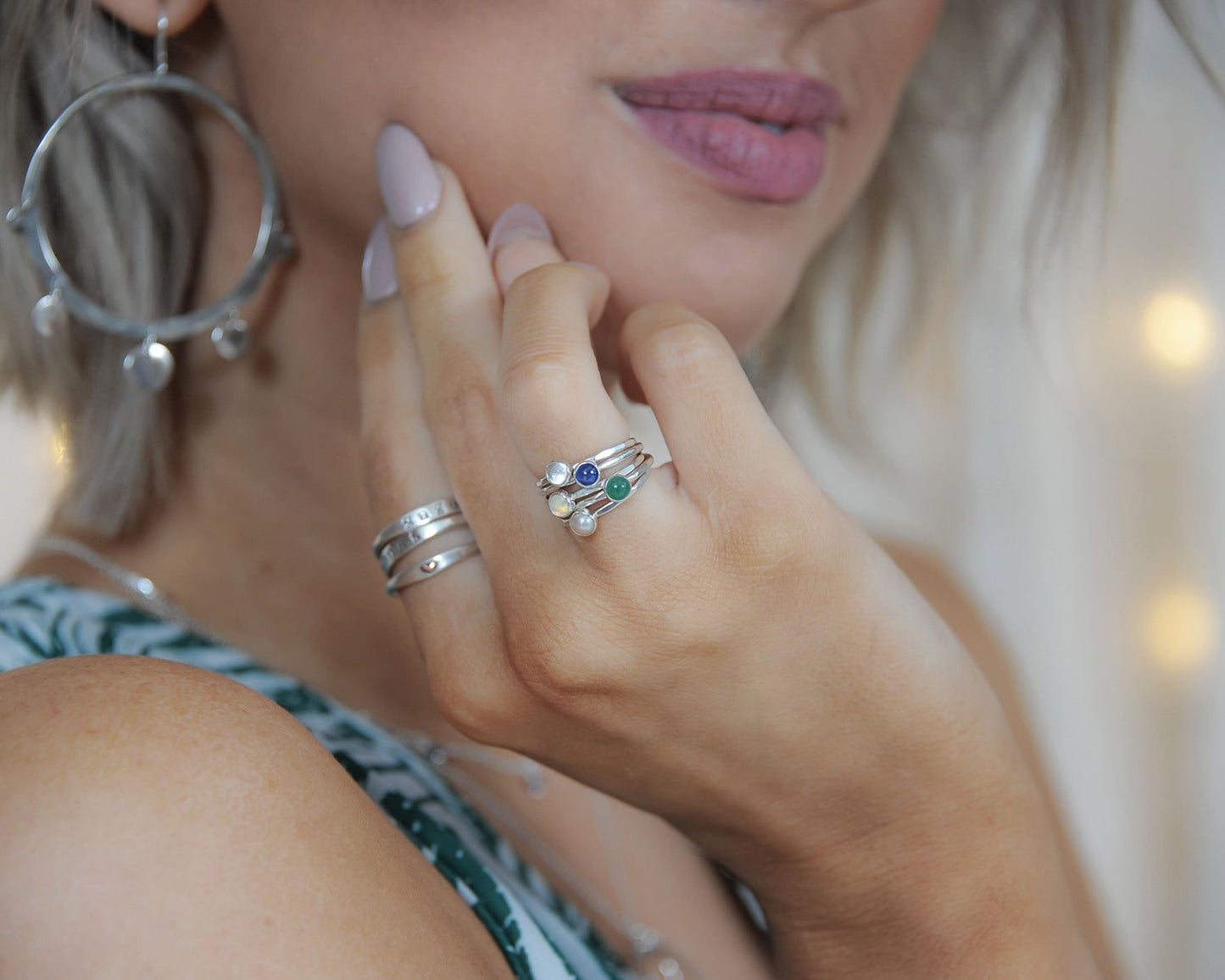 A close-up of a person's hand wearing multiple rings, including a ring with a gemstone and another ring with a floral design.