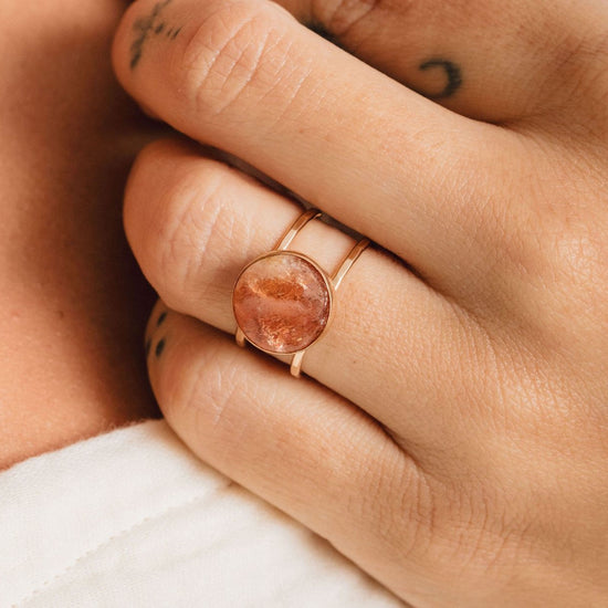 A close-up of a person's hand wearing a gold ring with a large, round stone in the center.