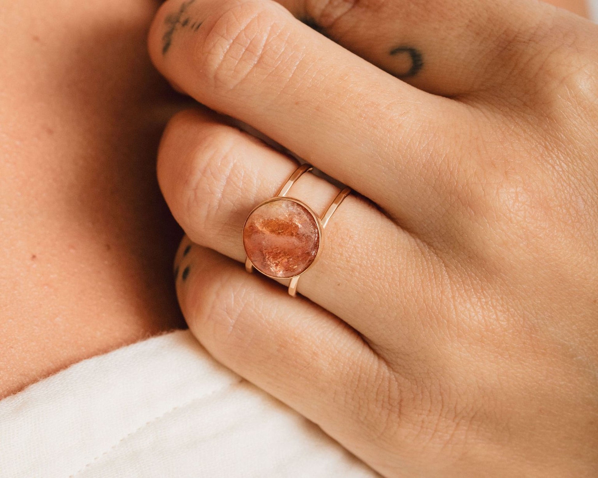 A close-up of a person's hand wearing a gold ring with a large, round stone in the center.