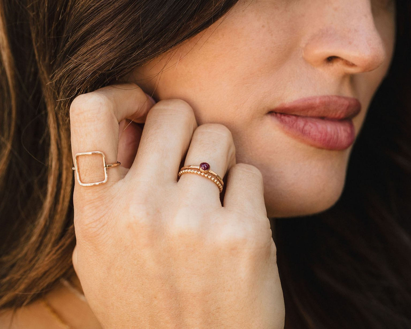 A close-up of a woman's face, focusing on her hand adorned with multiple rings.